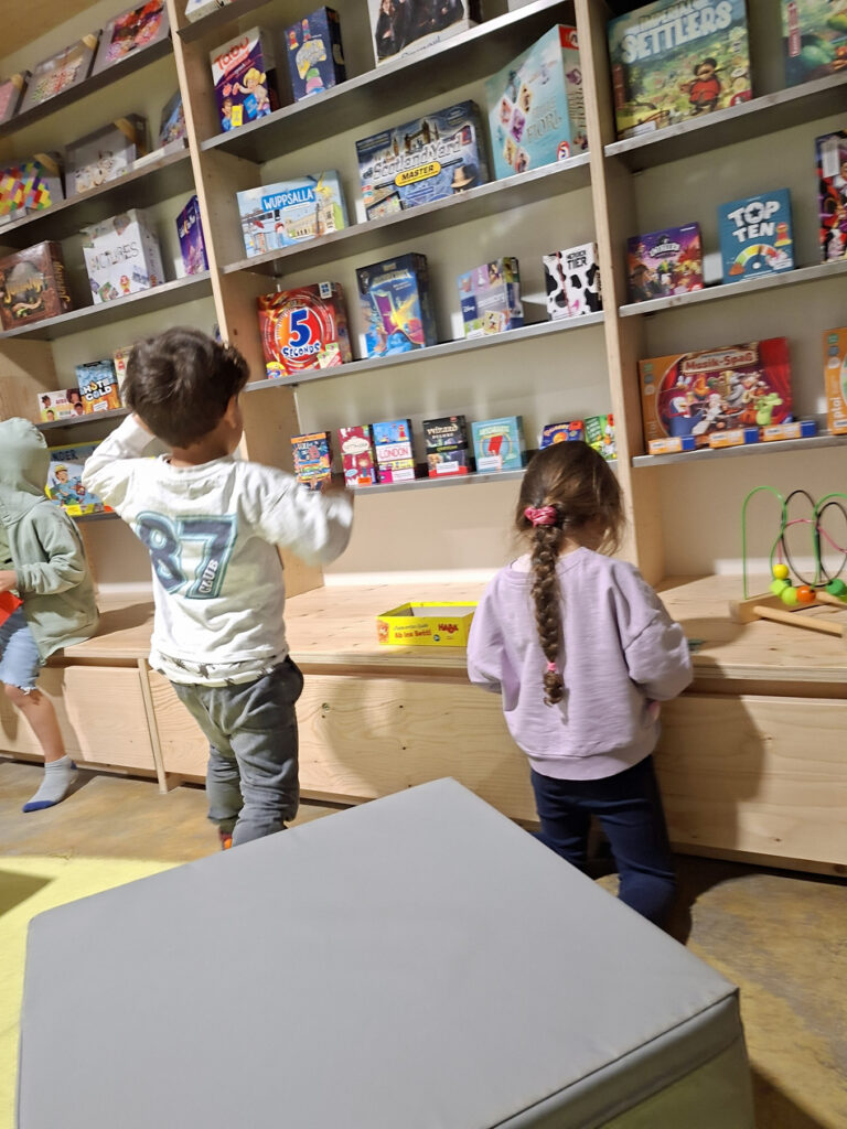 Kinder stehen vor einem grossen Holzregal mit Spielsachen