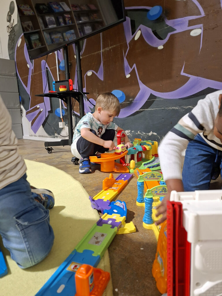 Aus bunten Schienenelementen bauen Kinder eine Bahn und lassen Fahrzeuge darauf fahren