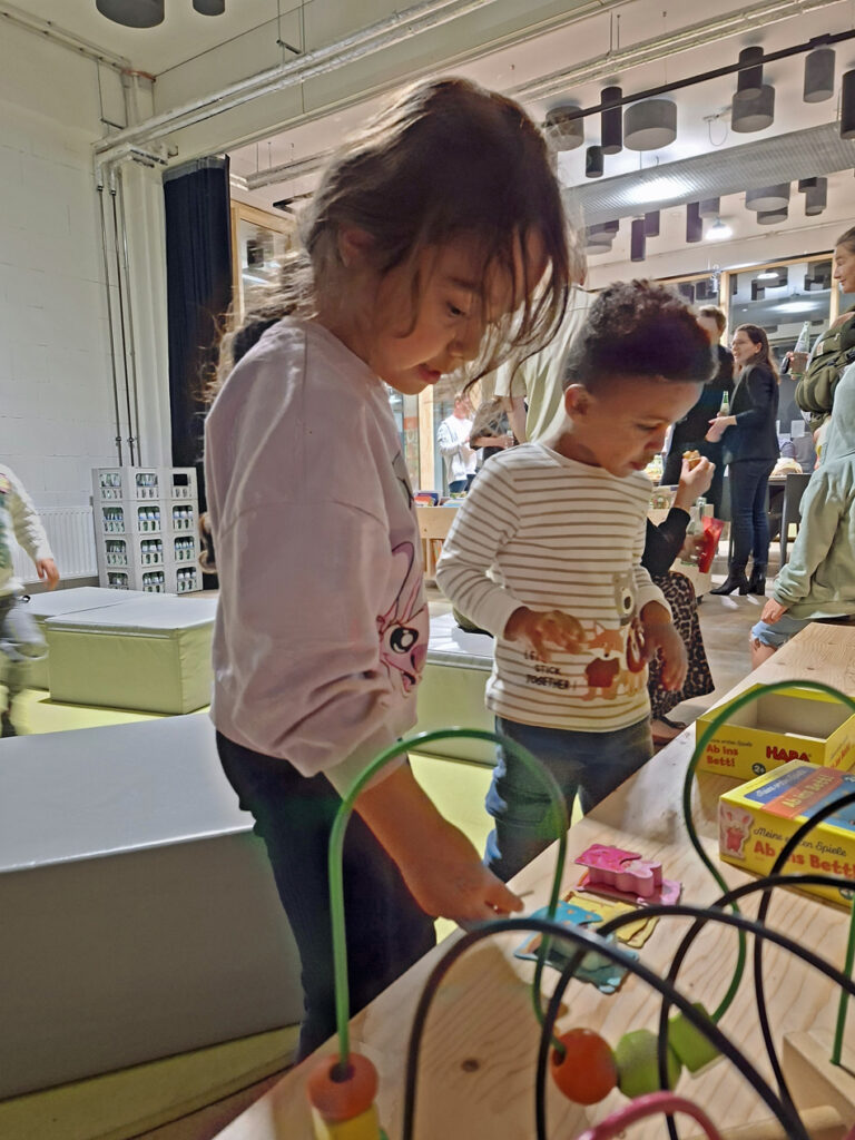 Kinder schauen sich in der Stadtteilbibliothek Spielsachen auf einem Holztisch an