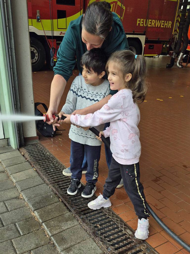 Kinder und eine Erzieherin spritzen Wasser aus einem Feuerwehrschlauch