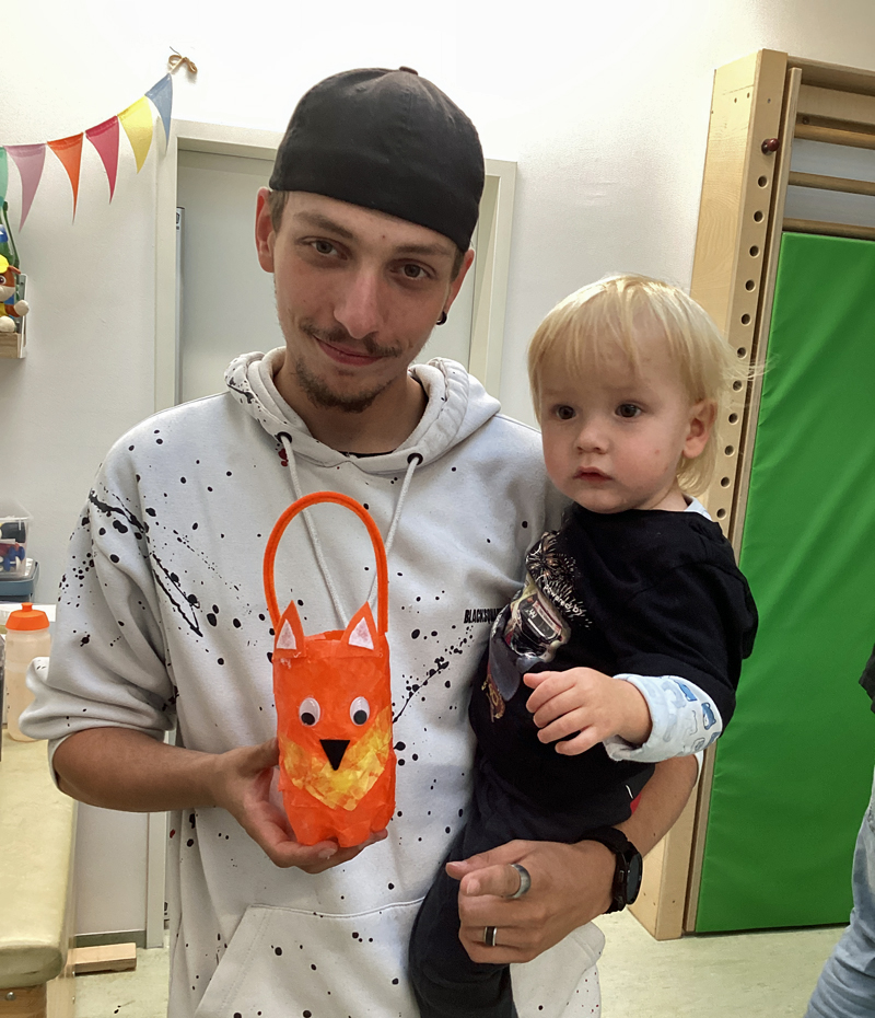 Ein Mann haelt ein Kind auf dem Arm und zeigt mit der anderen Hand eine rote Fuchs-Laterne