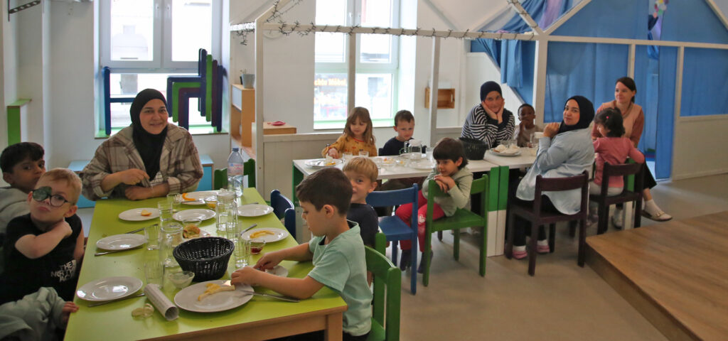 Zum Erntedankfruehstueck haben sich Erzieherinnen und Kinder an Tische gesetzt