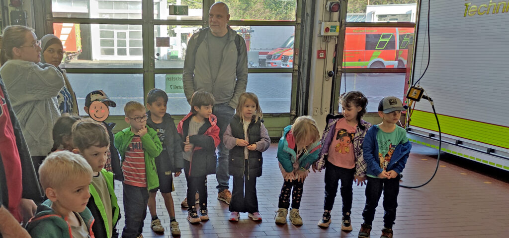 Eine Gruppe von Kindern und Erwachsenen steht im Feuerwehr Geraetehaus neben einem Fahrzeug