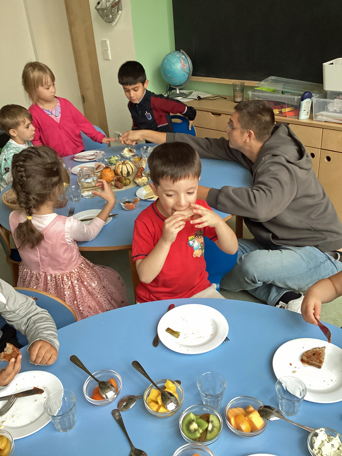Kinder und ein Erzieher fruehstuecken an einem reich gedeckten Tisch